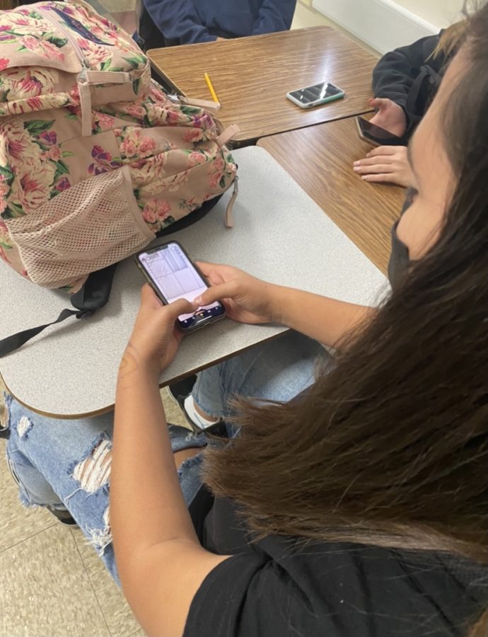 Freshman Isabella Brito hiding her Snapchat behind her backpack in Mr. Billers third period math class. Photo by: Brody Daw