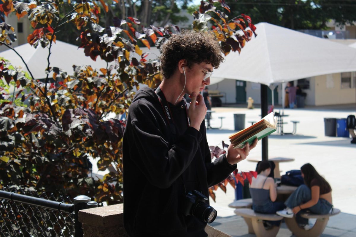 Noah Brace '28 reading "Little Women" while listening to Clairo with his wired earbuds. He is using non-prescription glasses. Photo by: Henry Hampton